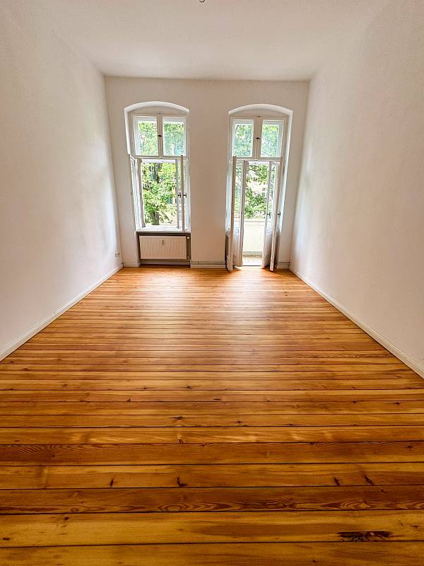 Altbauzimmer mit renoviertem Holzdielenboden und Fenster mit Balkontür am Ende