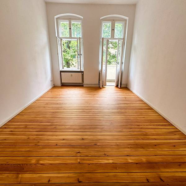 Altbauzimmer mit renoviertem Holzdielenboden und Fenster mit Balkontür am Ende