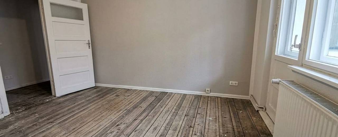 Abgenutzter, dunkler Holzdielenboden in einem leeren Raum vor der Renovierung.