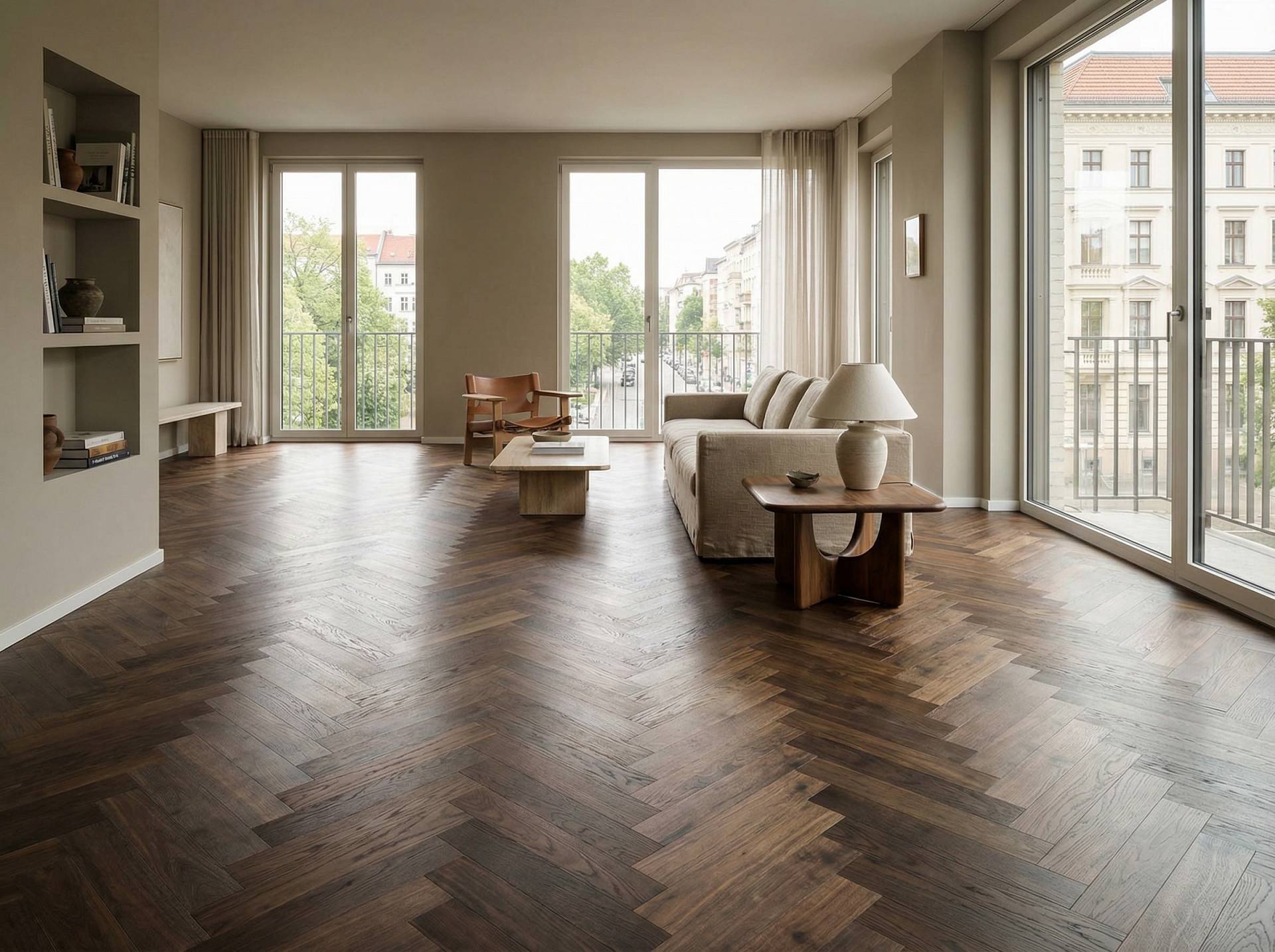 Ein heller Wohnraum mit großen Fenstern, eingerichtet mit Möbeln, und einem dunkel verlegten Fischgrätparkett aus Holz.