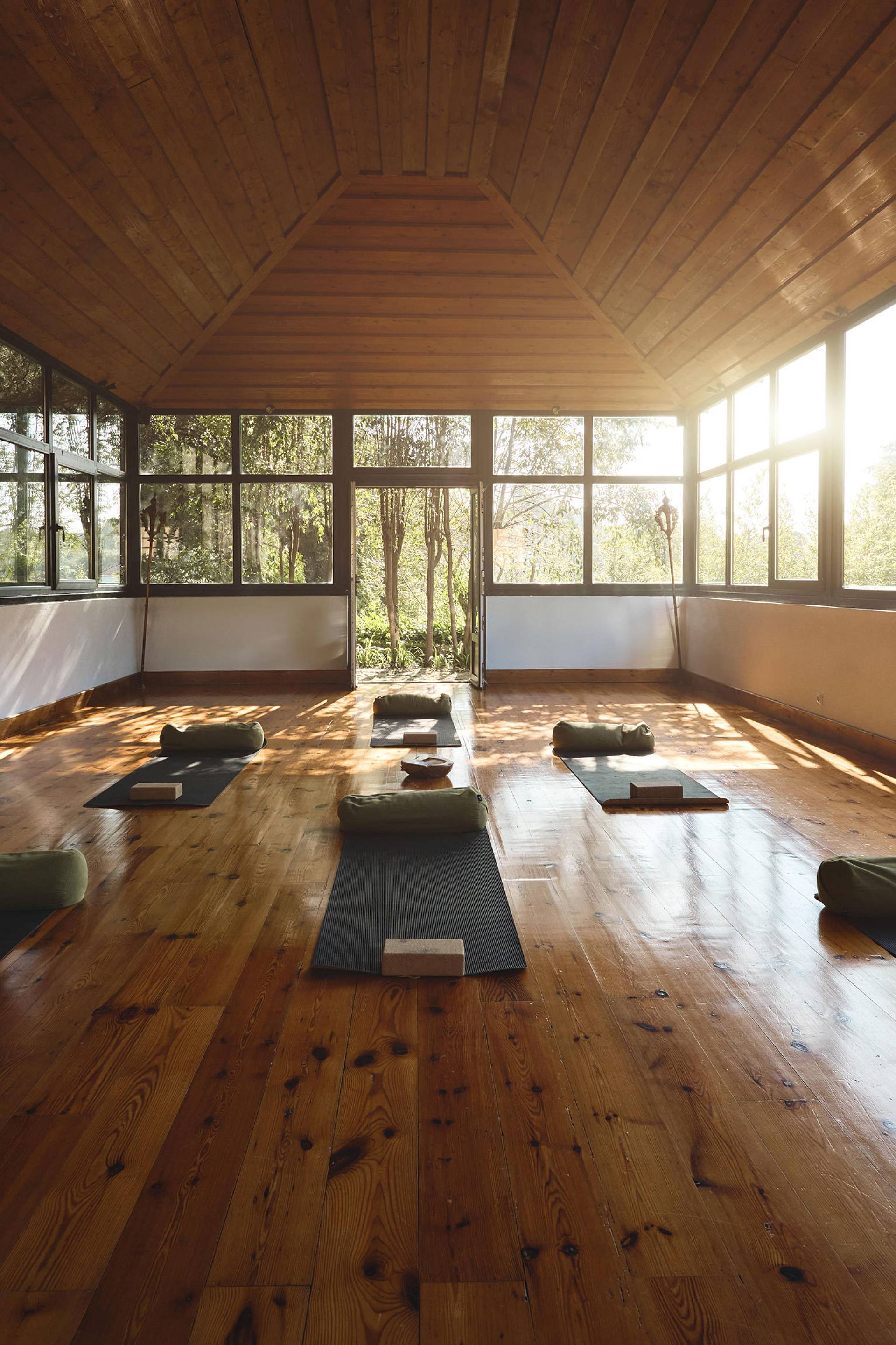 Heller Yogaraum mit Holzboden, Matten und großen Fenstern