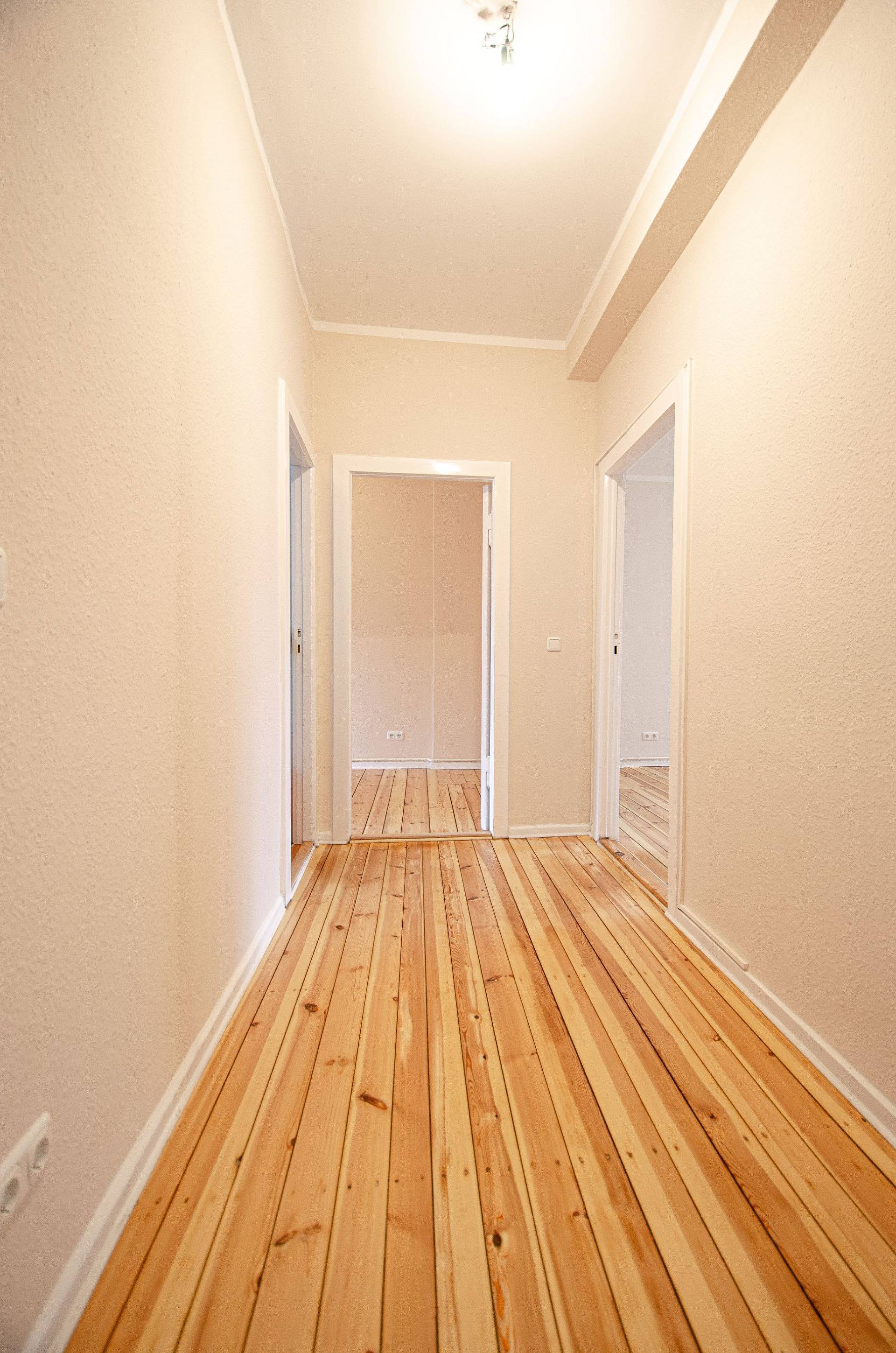 Helles, modernes Wohnzimmer mit breiten Holzdielen, Sofa, Sesseln, Couchtisch und großen Fenstern.