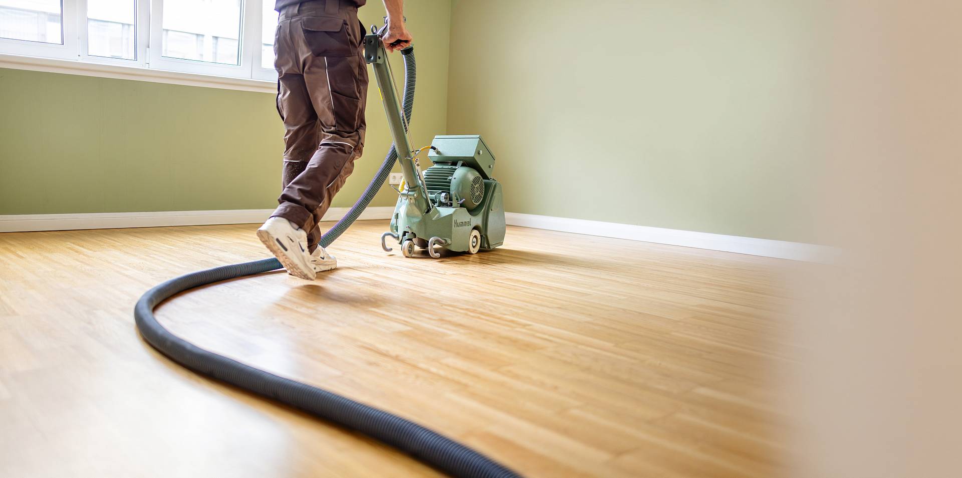 Handwerker schleift hellen Parkettboden mit Bodenschleifmaschine in leerem Raum