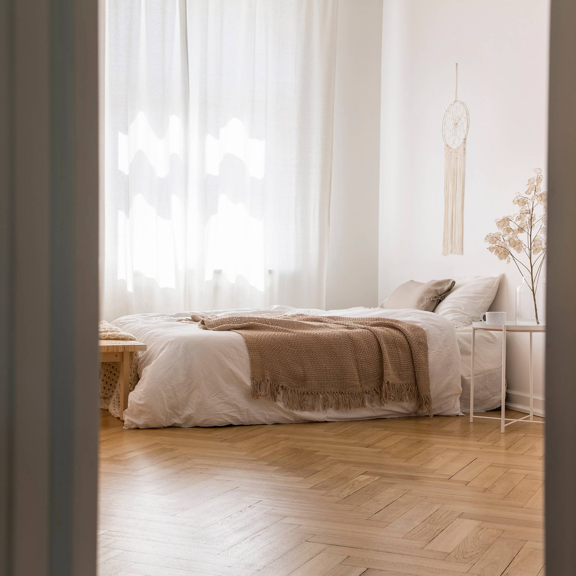 Helles Schlafzimmer mit Holzboden, Doppelbett, weißen Vorhängen, Wanddeko und sanftem Tageslicht