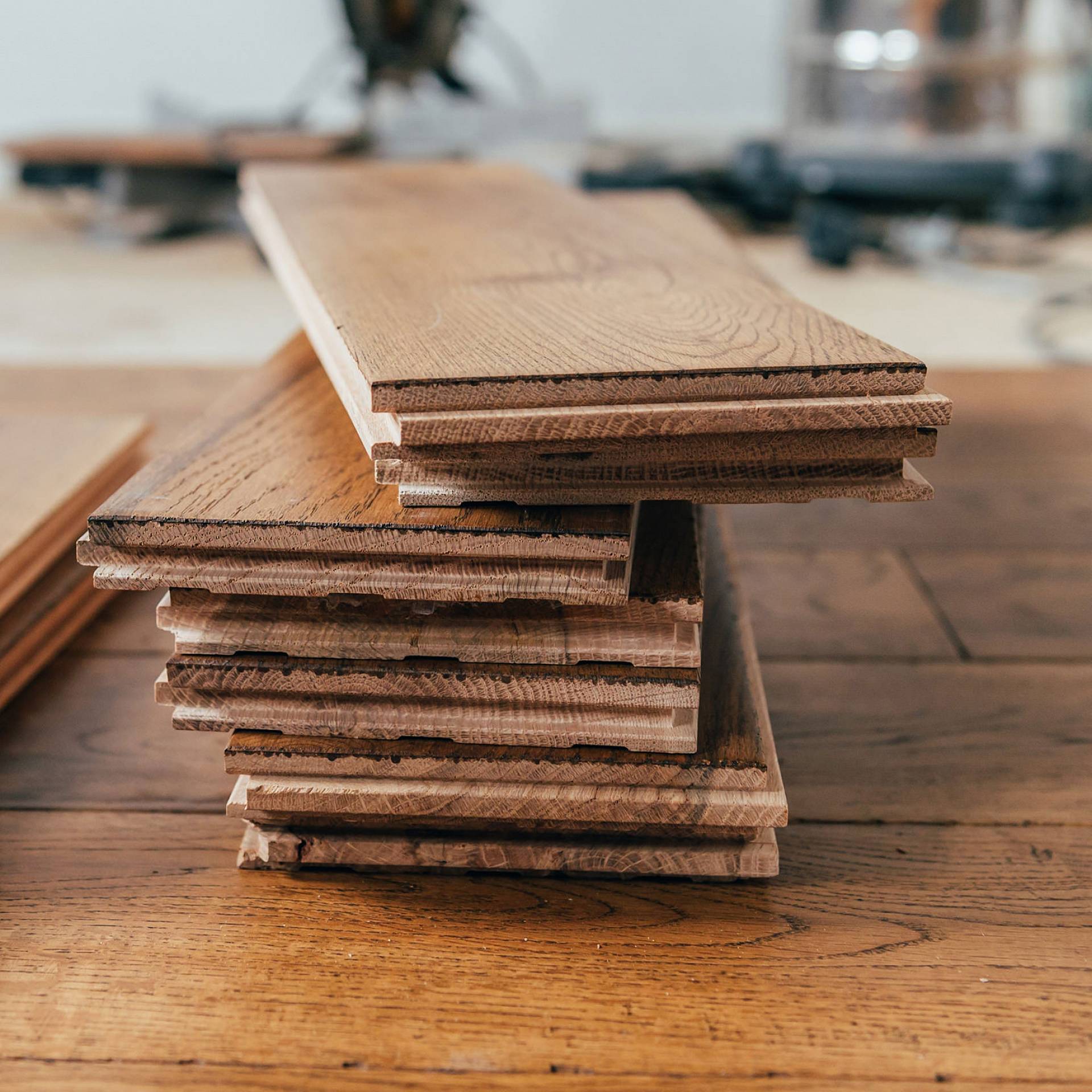 Gestapelte Holzplanken auf einer Werkbank in einer Werkstatt, mit sichtbarer Maserung und natürlicher Oberfläche.