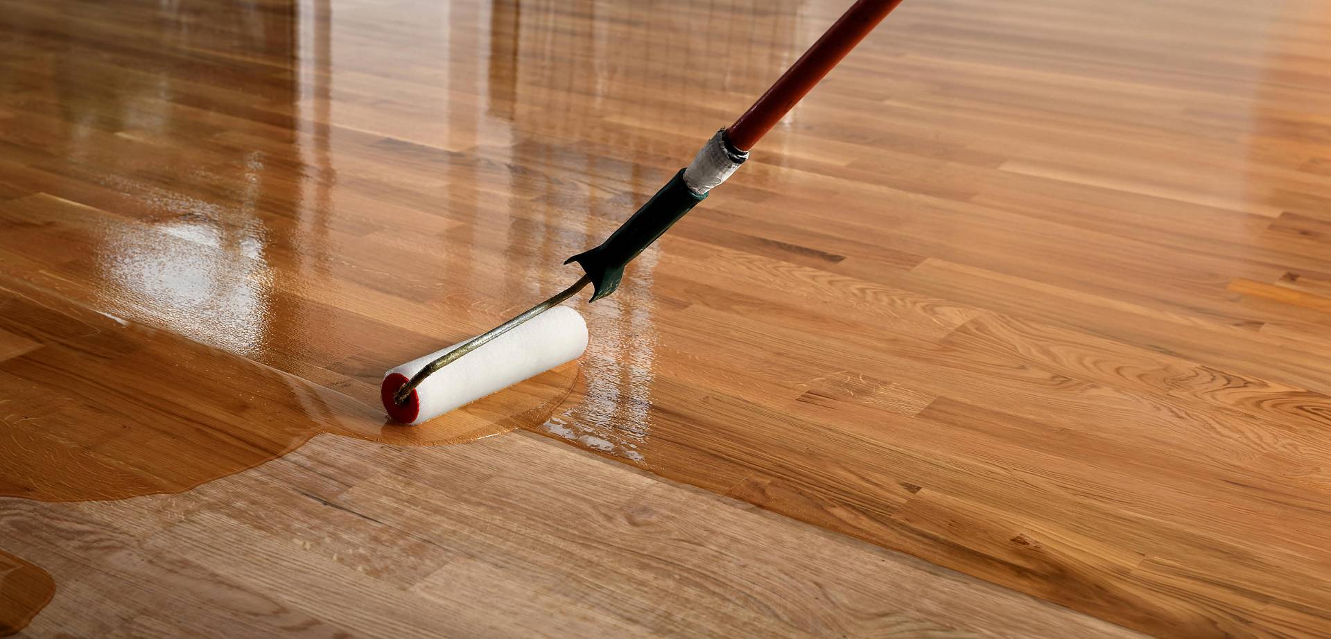 Lackrolle trägt glänzenden Klarlack auf einen Holzboden auf, wodurch eine gleichmäßige, spiegelnde Oberfläche entsteht.