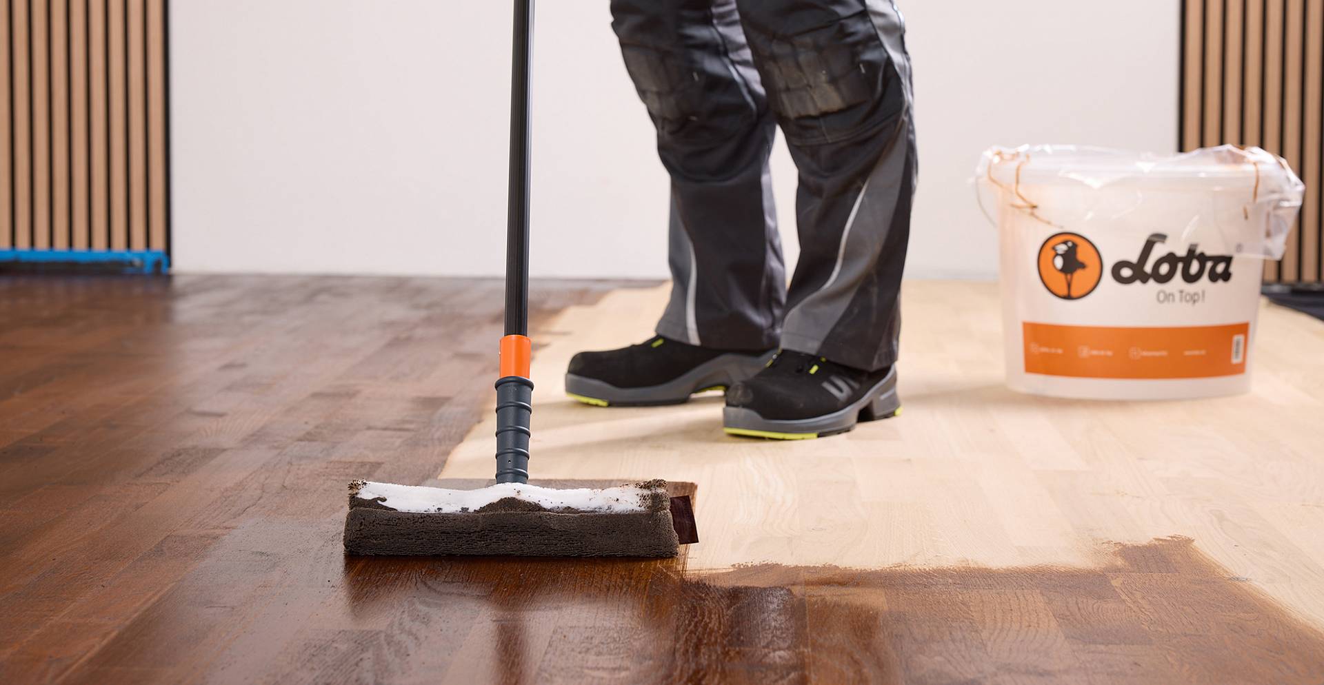 Handwerker färbt mit einer Schwammrolle einen hellen Parkettboden dunkel