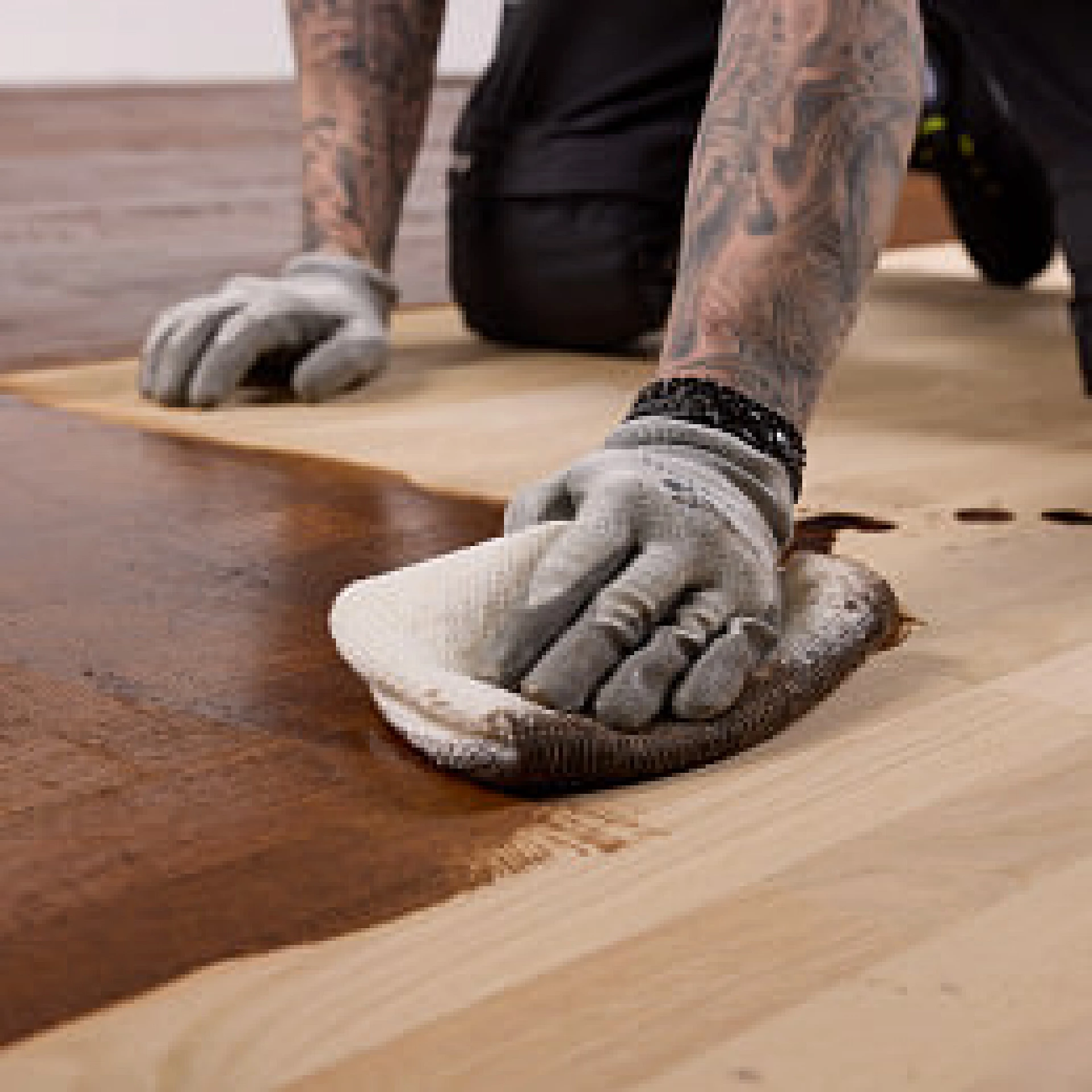 Hand trägt mit einem Microfasertuch braune Holzfarbe auf helle Holzdielen auf.
